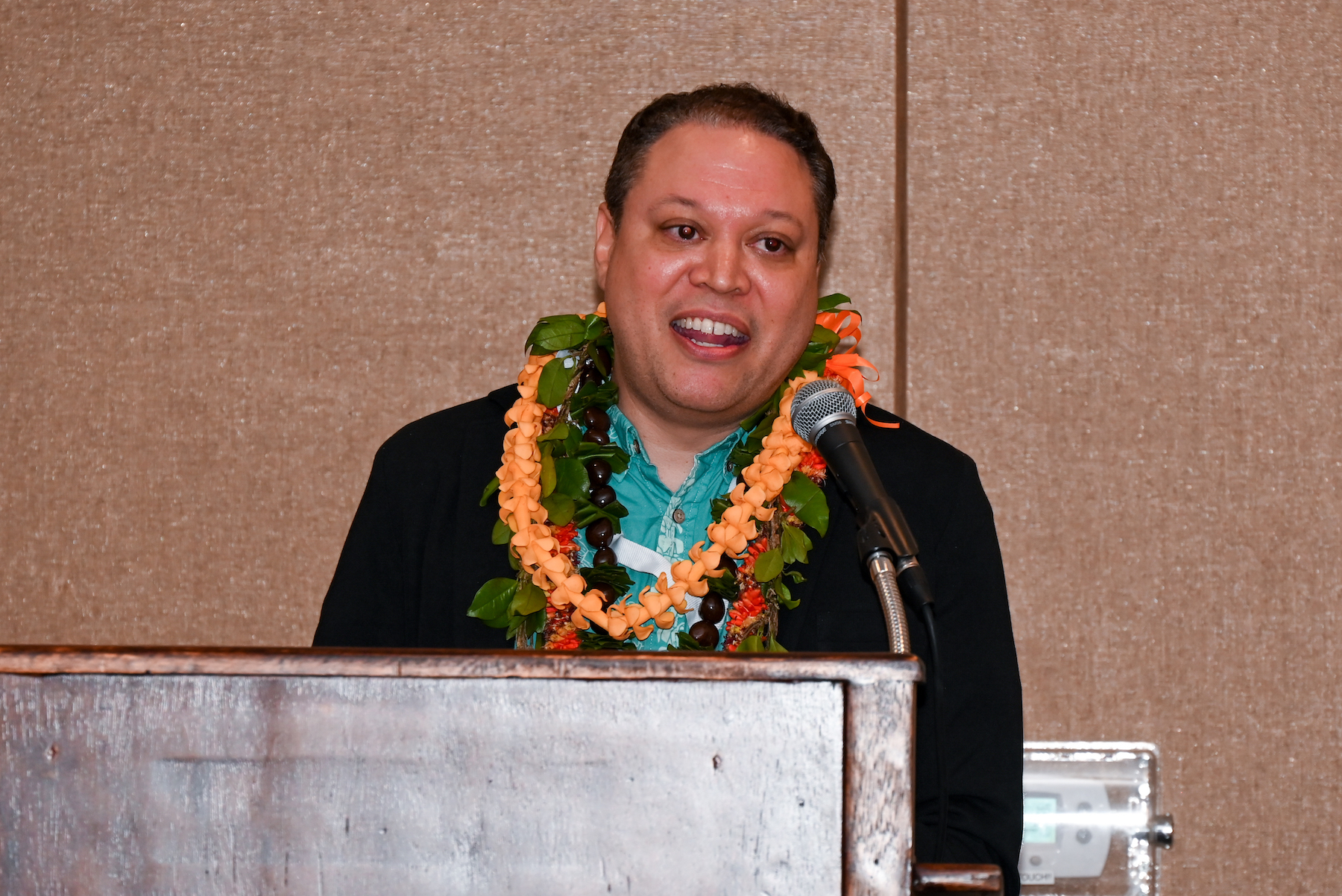 Dr. Alika Maunakea at podium wearing lei